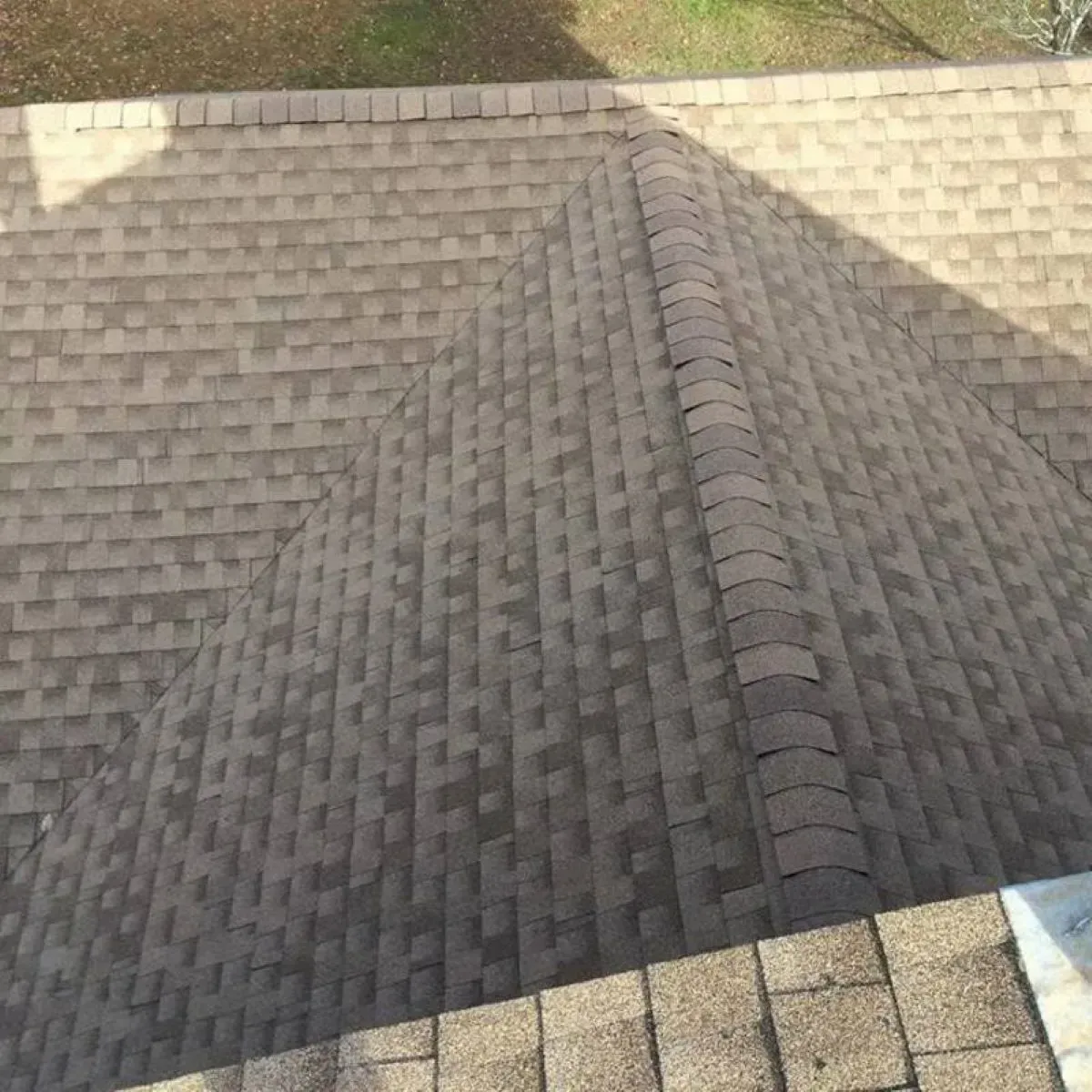 An overhead view of a brown shingled roof with a prominent ridge line and a diagonal shadow across one slope.