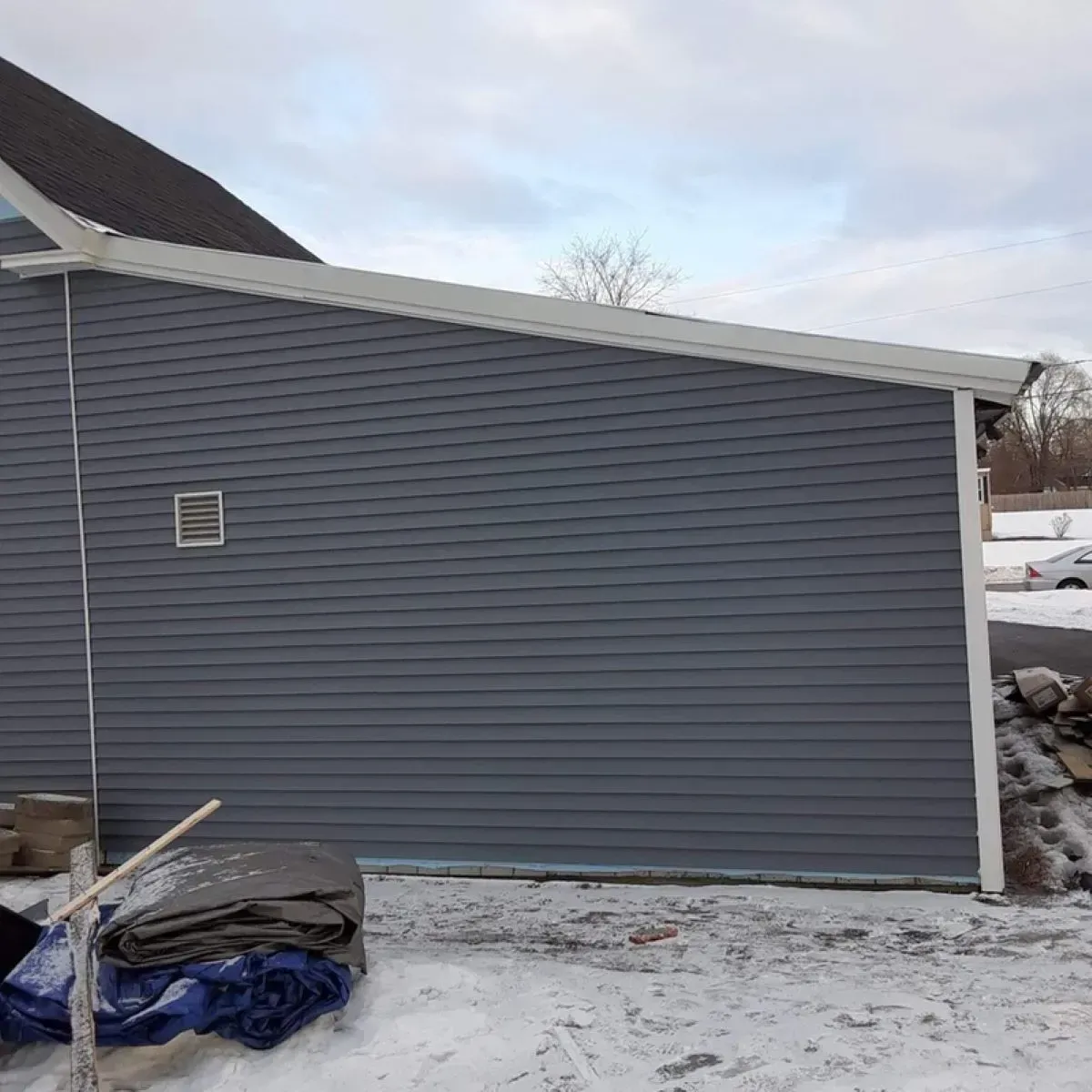 A gray, modern house stands with a sloped roof and white trim against a cloudy sky.