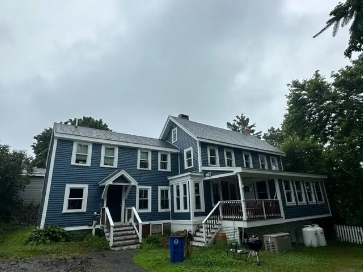 A blue, multi-story house with a porch stands beneath a cloudy sky.