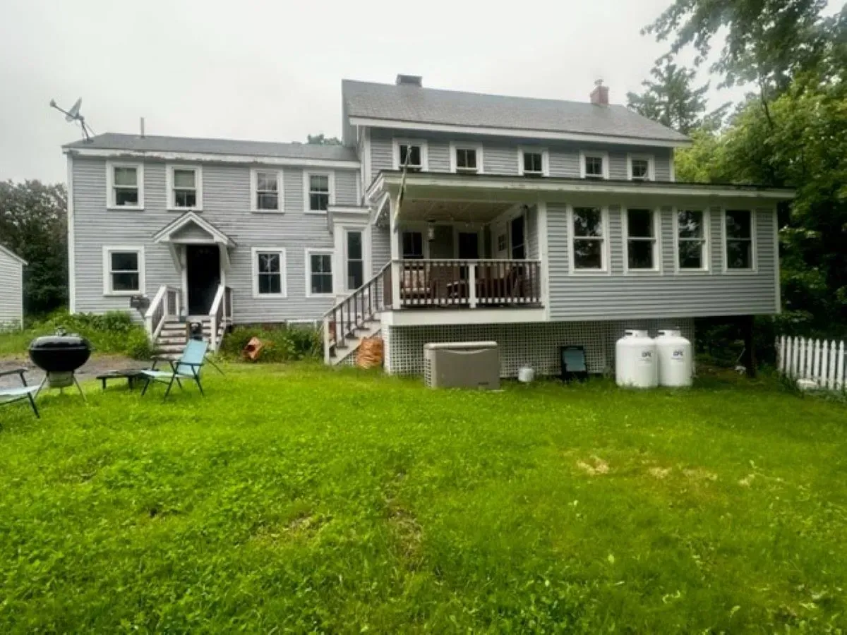 A large, gray house with a wrap-around porch sits on a well-maintained green lawn.
