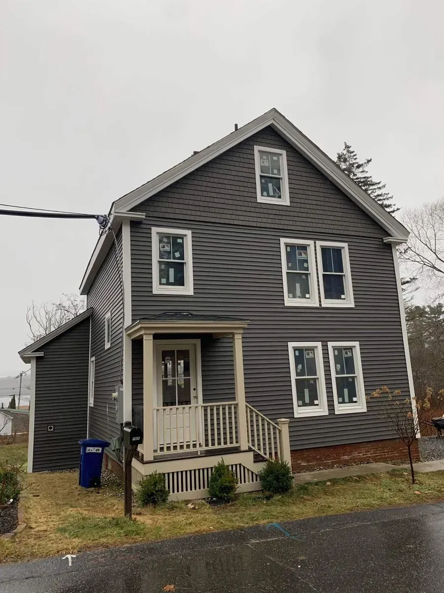 A two-story gray house with white trim and a small porch stands in a residential neighborhood.