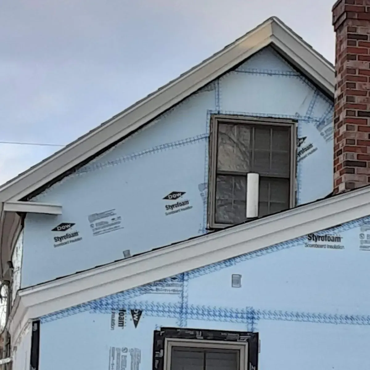 Gable end of a house under construction, covered in light blue Dow Styrofoam insulation with windows cut out.